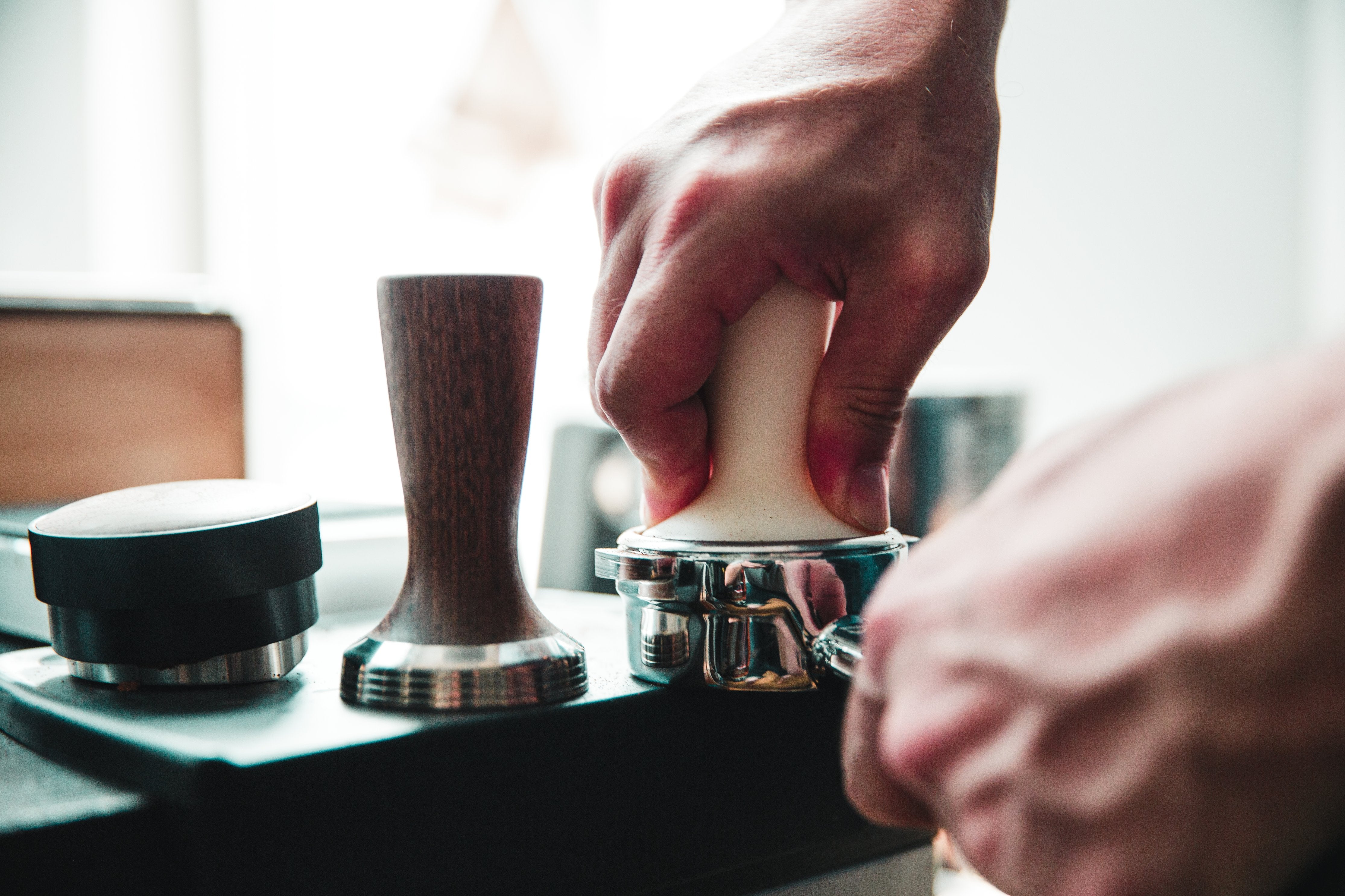 Barista tamping espresso grounds with a stainless steel coffee tamper